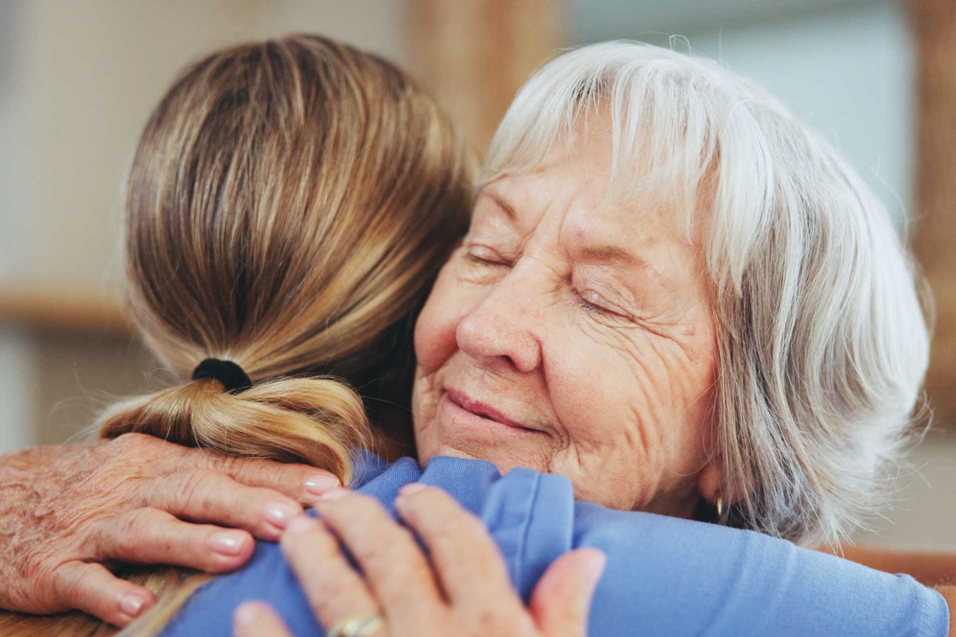An older woman embraces a young girl, both smiling warmly in a moment of affection
