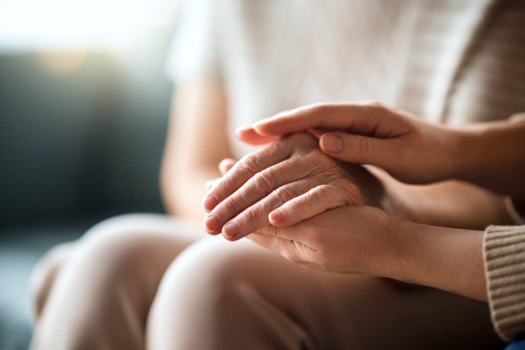 Close-up of one person gently holding another’s hands, offering comfort and reassurance in a softly lit, calm indoor setting