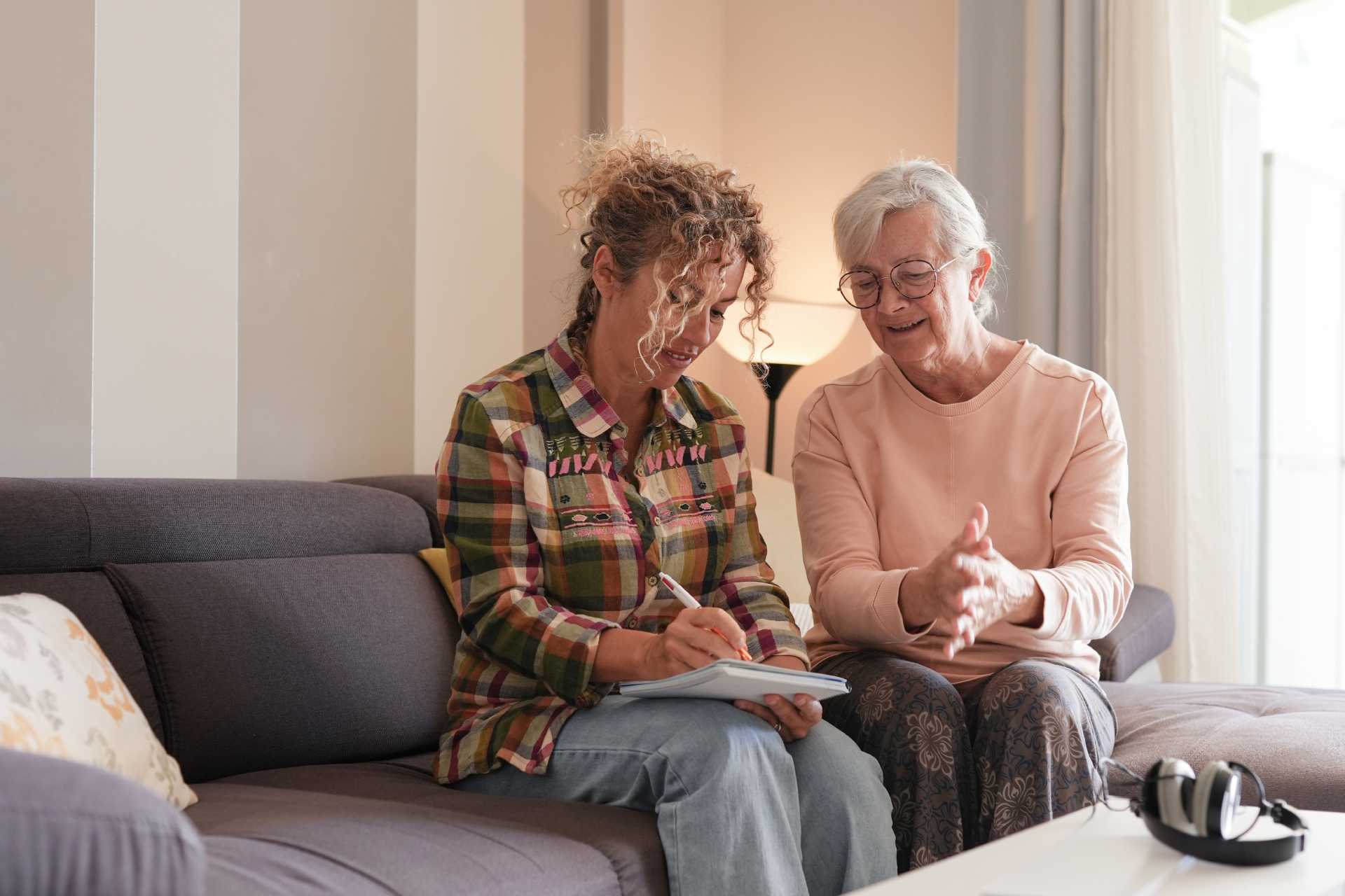 Two women sitting on a couch, engaged with a tablet, sharing ideas and enjoying each other's company
