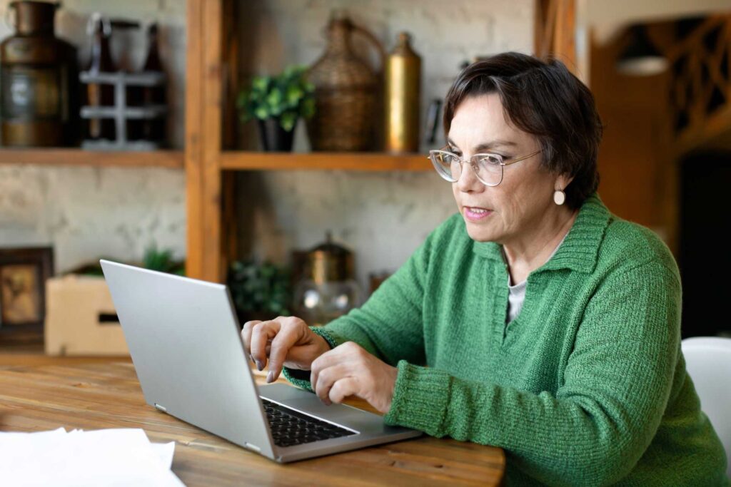 Elderly Woman Works In Front Of A Laptop Monitor With